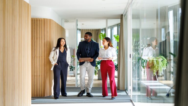 A diverse group of business professionals walks through a modern office corridor. This group reflects teamwork and collaboration in a corporate environment, showcasing commitment and communication.